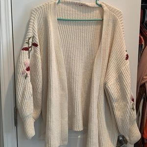 White cardigan with flower embroidery on sleeve.